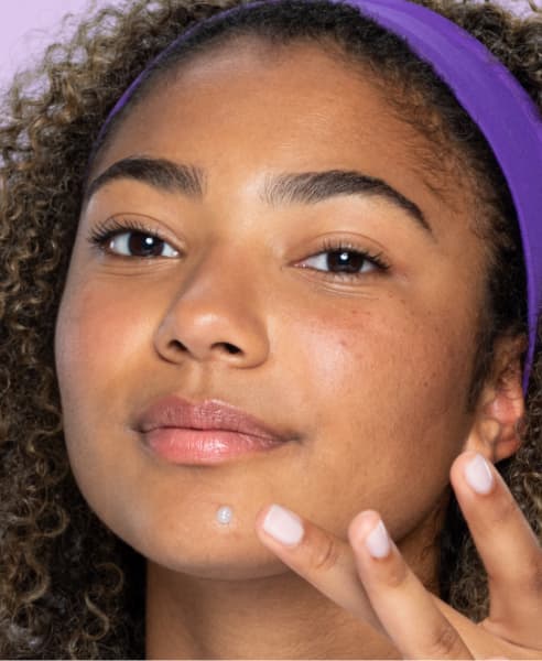 teen with purple headband applying spot cream to chin
